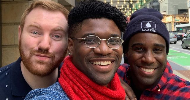 Tramell Tillman in a red and black check shirt smiling with his friends.